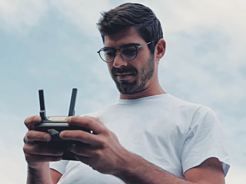 homme avec des lunettes et un t-shirt blanc qui regarde une manette de drone